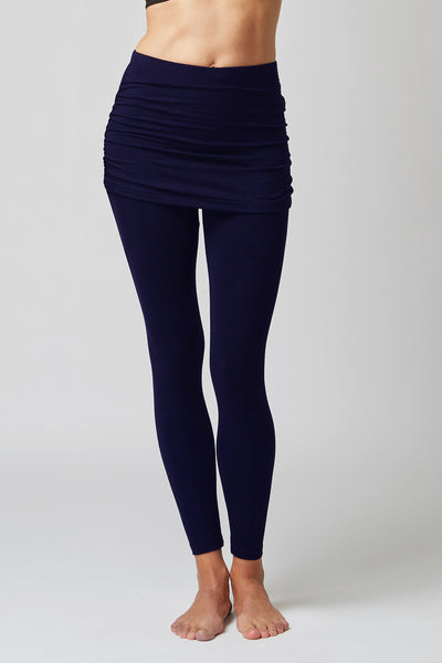 A person stands barefoot wearing the TLC Sport Medium Compression Waisted Leggings with Gathered Skirt in Navy, featuring a supportive waistband and high-waisted design, shown from midriff to feet against a plain light background.